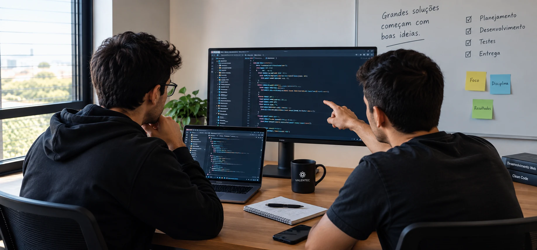 Dois desenvolvedores da Valentec revisando código juntos em frente ao monitor